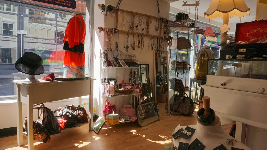 A well-lit vintage boutique showcasing clothing, bags, hats, and accessories.